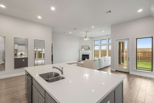 kitchen with a kitchen island with sink, gray cabinetry, sink, ceiling fan, and dishwasher