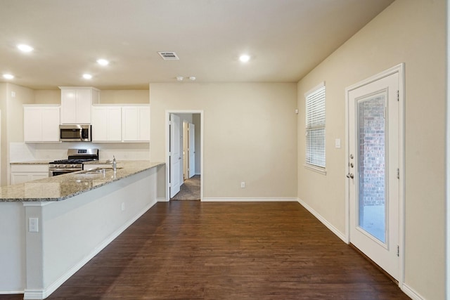 kitchen with kitchen peninsula, dark hardwood / wood-style flooring, light stone counters, appliances with stainless steel finishes, and white cabinets