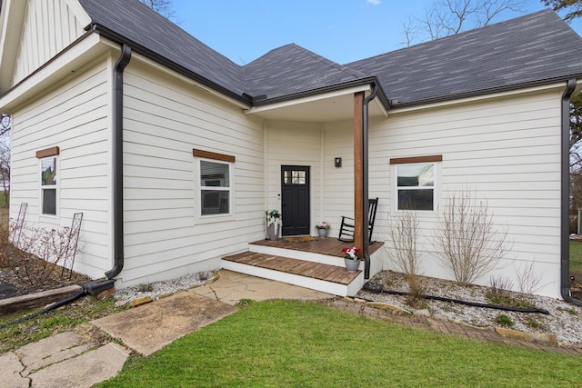 view of exterior entry featuring roof with shingles and a yard