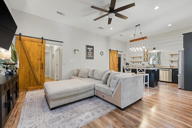 living area with light wood finished floors, recessed lighting, visible vents, a barn door, and ceiling fan