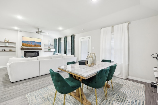 dining area with light wood-type flooring, lofted ceiling, ceiling fan, and built in features