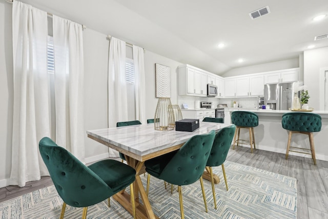 dining area with lofted ceiling, a wealth of natural light, and light hardwood / wood-style flooring