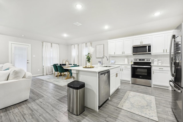 kitchen with sink, stainless steel appliances, white cabinets, an island with sink, and decorative backsplash