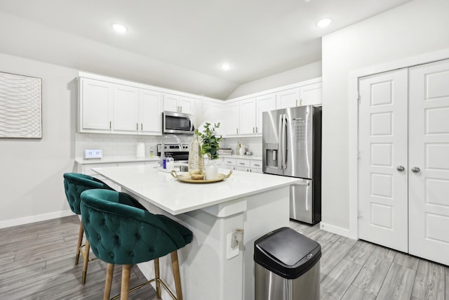 kitchen with stainless steel appliances, white cabinets, an island with sink, a breakfast bar area, and tasteful backsplash