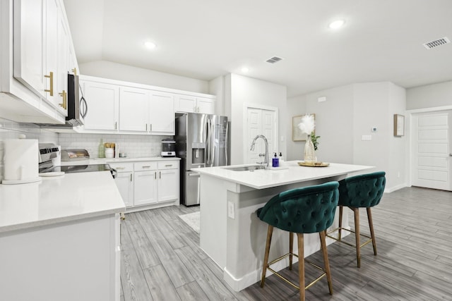 kitchen with appliances with stainless steel finishes, white cabinets, a breakfast bar, sink, and a kitchen island with sink