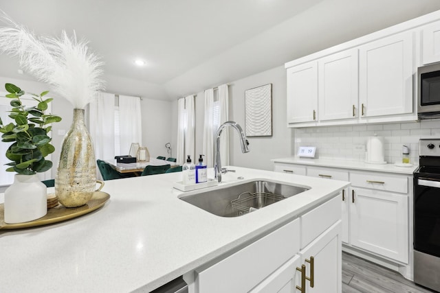 kitchen with appliances with stainless steel finishes, sink, backsplash, white cabinetry, and light hardwood / wood-style floors