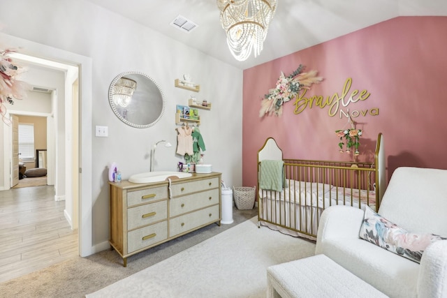 carpeted bedroom with a crib, vaulted ceiling, sink, and a notable chandelier