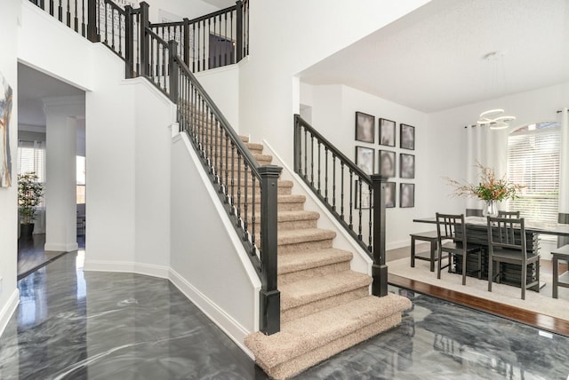 staircase with a towering ceiling, baseboards, and a notable chandelier