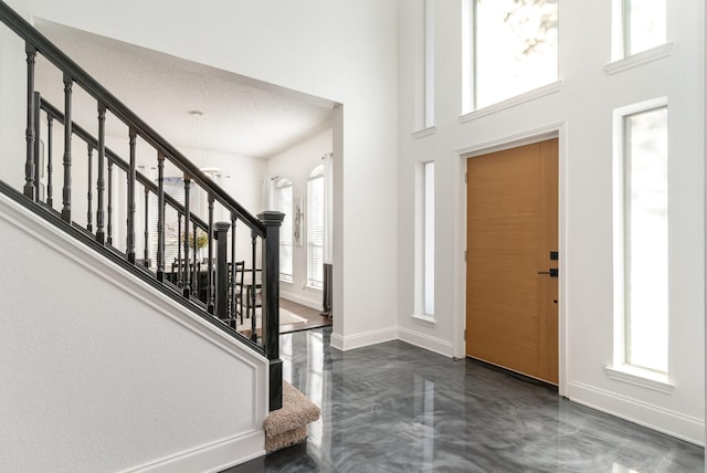 entryway featuring finished concrete floors, a towering ceiling, stairway, and baseboards