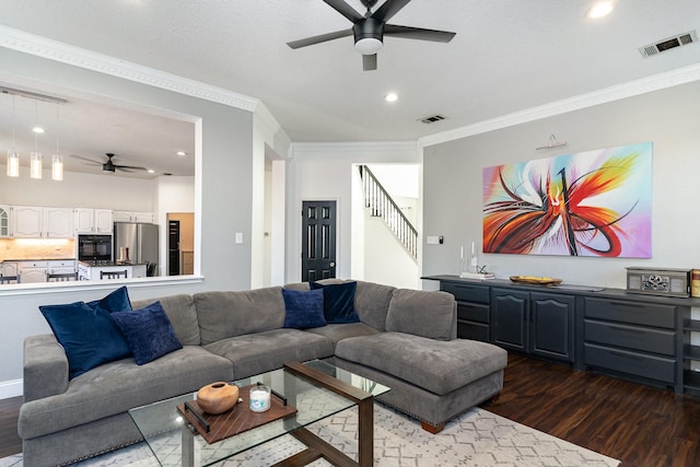 living room with crown molding, dark wood-type flooring, visible vents, and a ceiling fan