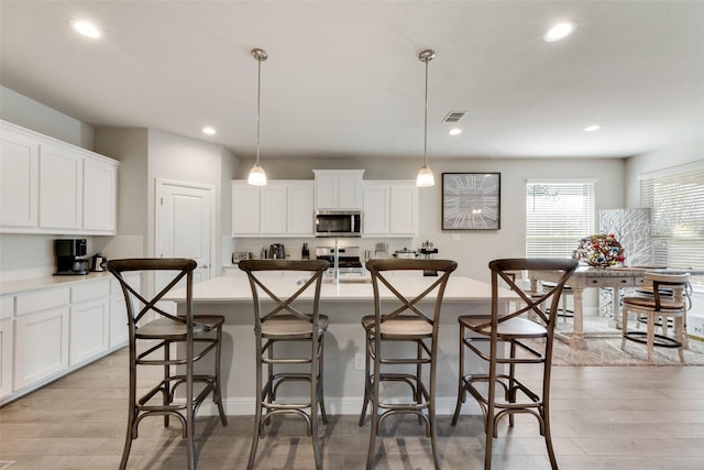 kitchen featuring a center island with sink, stainless steel appliances, and decorative light fixtures