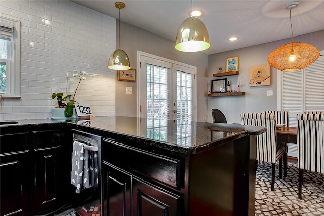 kitchen featuring dishwashing machine, french doors, dark stone counters, decorative backsplash, and pendant lighting