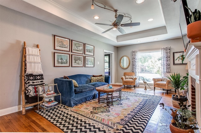 living room featuring a fireplace, ornamental molding, a raised ceiling, and hardwood / wood-style floors