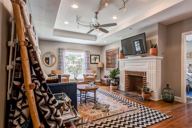 living area with wood-type flooring, crown molding, ceiling fan, a fireplace, and a raised ceiling