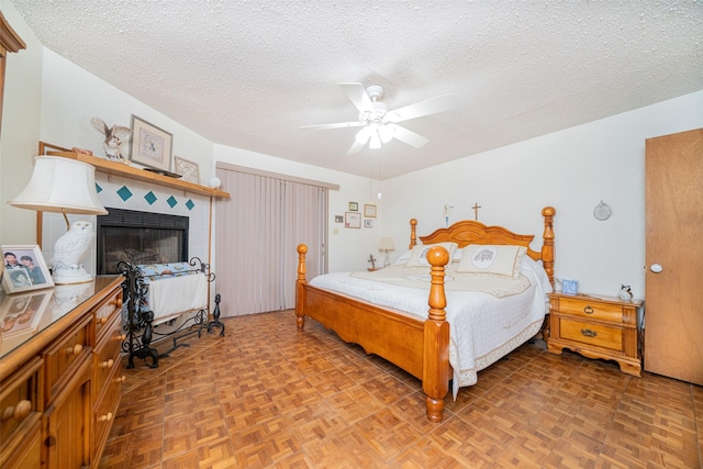 bedroom featuring a textured ceiling, ceiling fan, parquet floors, and a fireplace