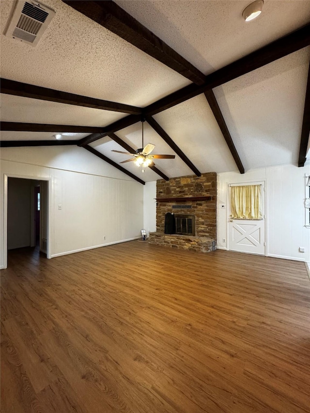 unfurnished living room with dark hardwood / wood-style flooring, a stone fireplace, vaulted ceiling with beams, ceiling fan, and a textured ceiling