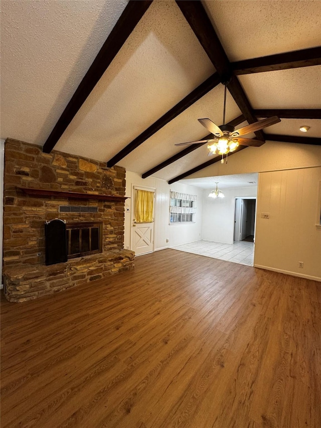 unfurnished living room featuring light wood-type flooring, vaulted ceiling with beams, a stone fireplace, and a textured ceiling