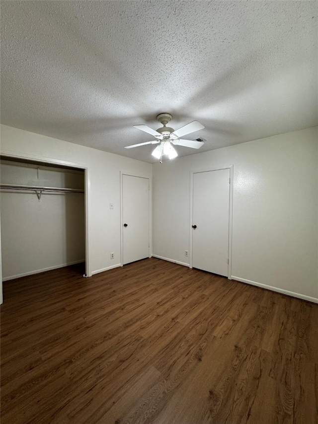 unfurnished bedroom featuring dark hardwood / wood-style flooring, multiple closets, a textured ceiling, and ceiling fan