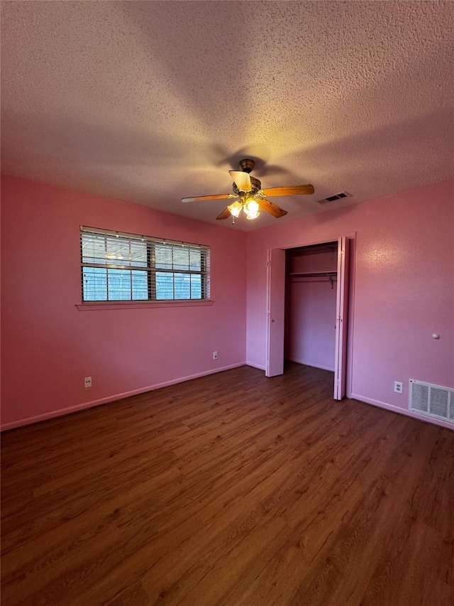 unfurnished bedroom featuring ceiling fan, a closet, dark wood-type flooring, and a textured ceiling