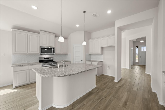 kitchen featuring visible vents, a center island with sink, a sink, backsplash, and appliances with stainless steel finishes