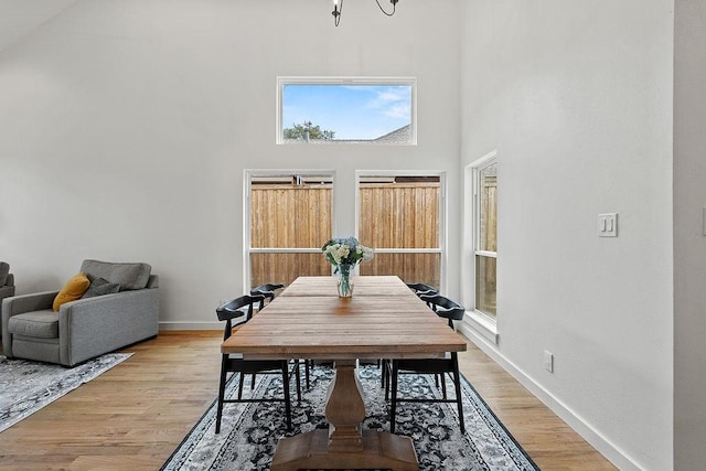 dining room with baseboards, a towering ceiling, and light wood-style floors