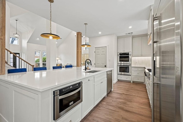 kitchen featuring a sink, hanging light fixtures, light countertops, appliances with stainless steel finishes, and an island with sink