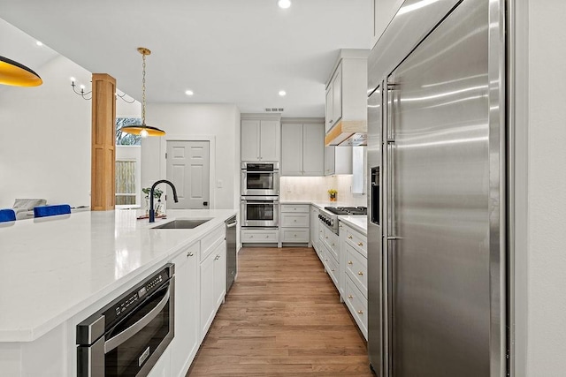 kitchen featuring decorative light fixtures, appliances with stainless steel finishes, white cabinetry, a sink, and an island with sink