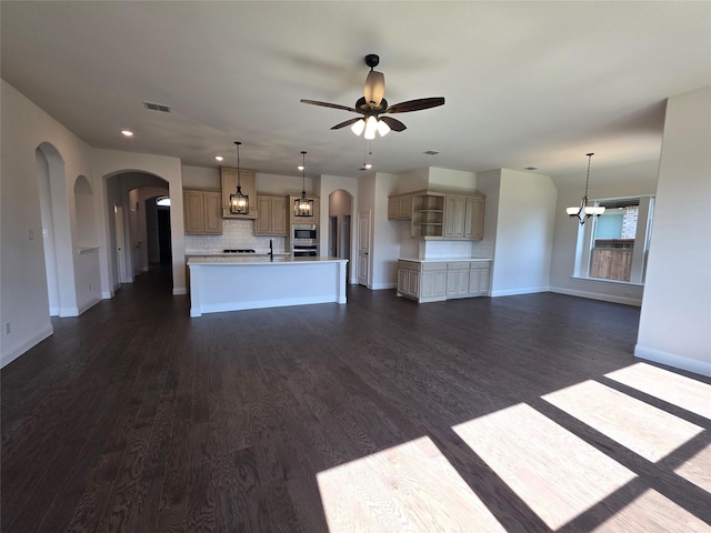 unfurnished living room with ceiling fan with notable chandelier, arched walkways, baseboards, dark wood-style flooring, and visible vents