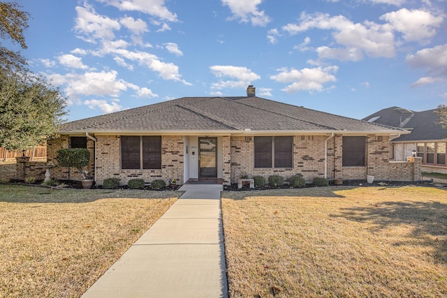 view of front of property featuring a shingled roof, a front yard, brick siding, and a chimney