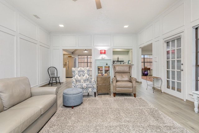 sitting room with ornamental molding, a ceiling fan, light wood-style flooring, and a decorative wall