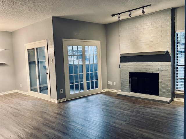 unfurnished living room featuring dark wood-style floors, a fireplace, a wealth of natural light, and a textured ceiling