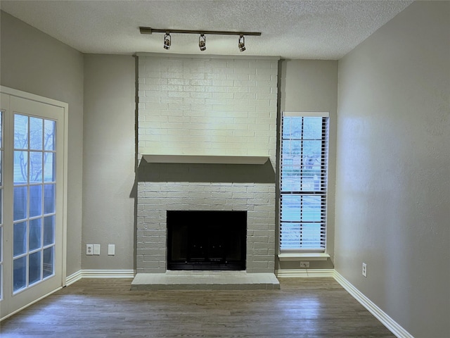 unfurnished living room with baseboards, wood finished floors, a textured ceiling, a brick fireplace, and track lighting