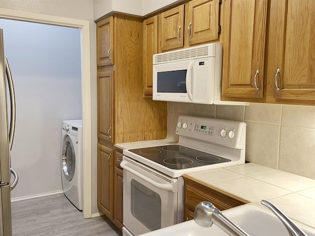 kitchen featuring white appliances, tasteful backsplash, brown cabinetry, and washer / dryer