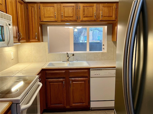 kitchen with tile counters, white appliances, a sink, and backsplash