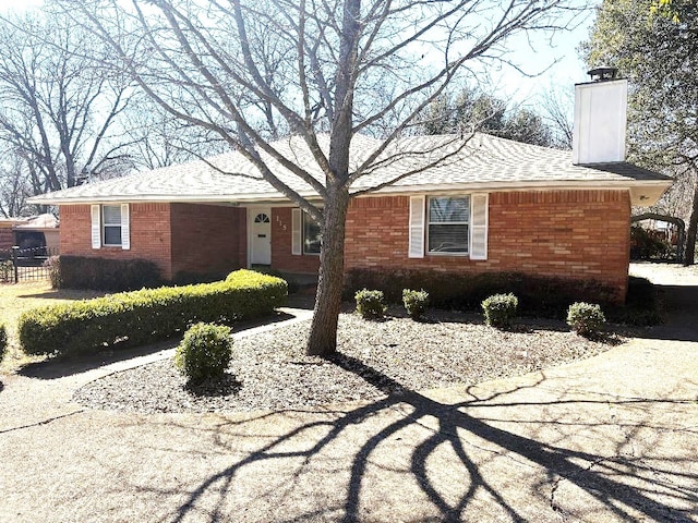 single story home with a shingled roof, brick siding, and a chimney