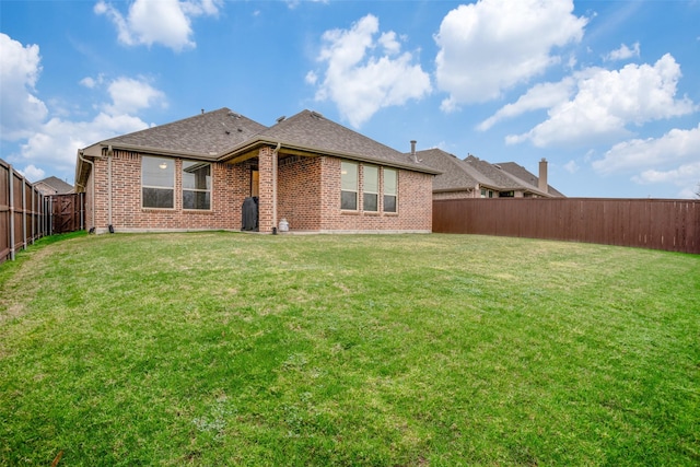 back of property featuring a yard, brick siding, a shingled roof, and a fenced backyard