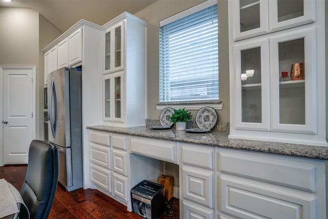 kitchen featuring dark wood-style floors, glass insert cabinets, light stone counters, freestanding refrigerator, and white cabinetry