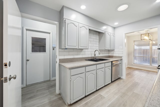 kitchen with decorative backsplash, dishwasher, light countertops, light wood-style floors, and a sink