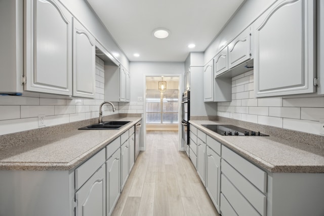 kitchen featuring dishwasher, black electric cooktop, light countertops, double oven, and a sink