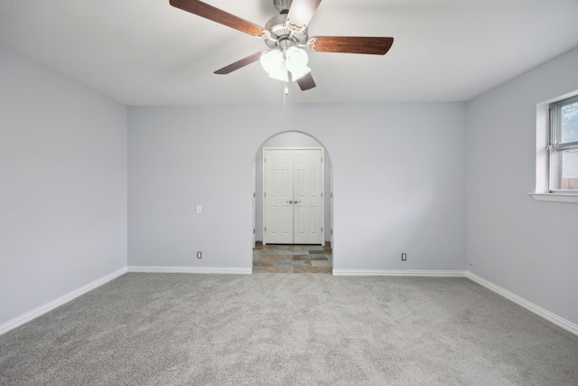 spare room with arched walkways, light carpet, ceiling fan, and baseboards