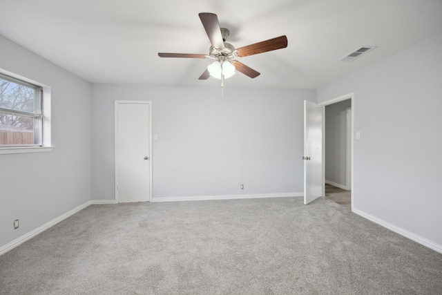 carpeted empty room with baseboards, visible vents, and a ceiling fan