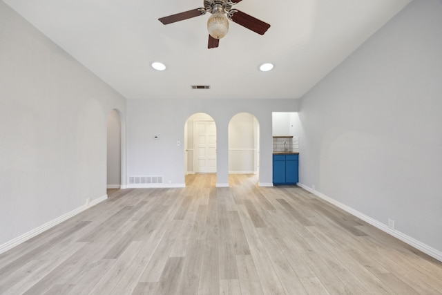 unfurnished living room with light wood-type flooring, visible vents, arched walkways, and baseboards