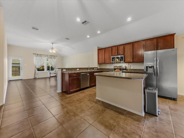 kitchen with dark stone counters, stainless steel appliances, a center island, and lofted ceiling