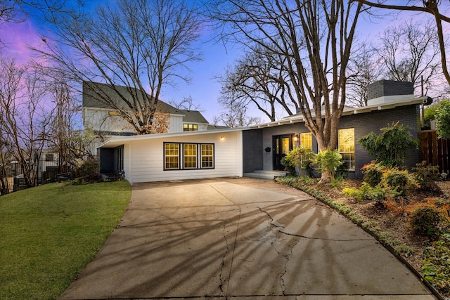 mid-century modern home featuring brick siding, a chimney, concrete driveway, fence, and a front lawn