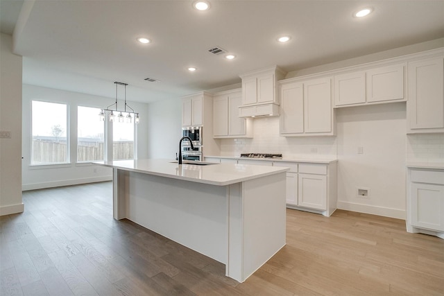 kitchen with hanging light fixtures, an island with sink, stainless steel appliances, sink, and white cabinetry