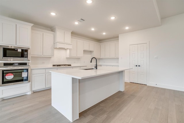 kitchen featuring sink, white cabinets, stainless steel appliances, and an island with sink