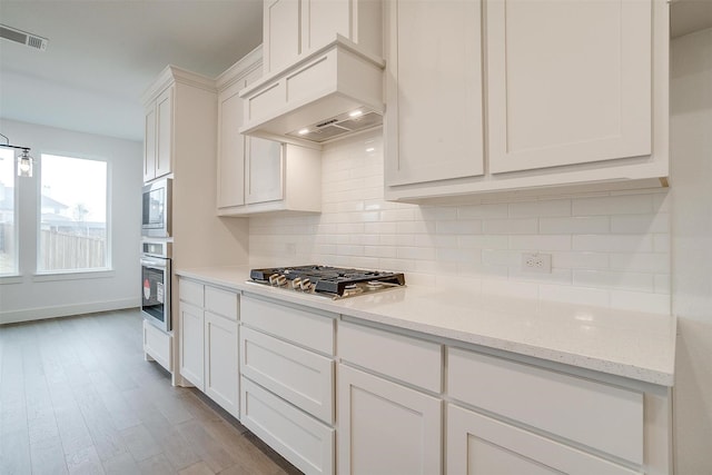 kitchen featuring stainless steel appliances, premium range hood, backsplash, light stone counters, and white cabinets