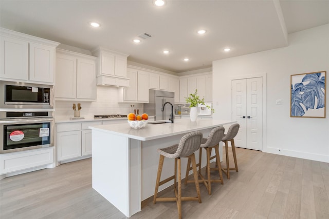 kitchen featuring built in appliances, sink, a kitchen island with sink, and white cabinets