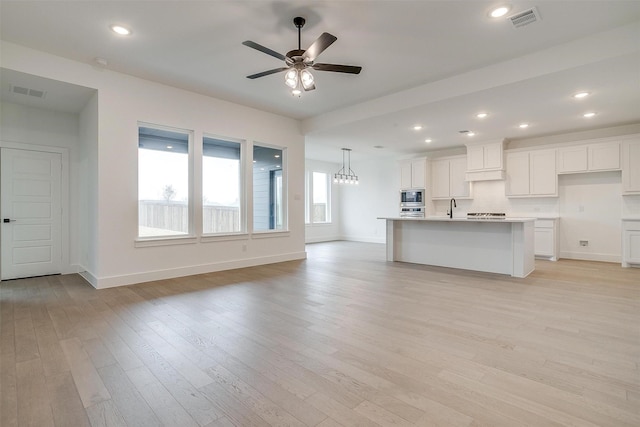 kitchen with a center island with sink, white cabinetry, ceiling fan with notable chandelier, light hardwood / wood-style floors, and stainless steel appliances