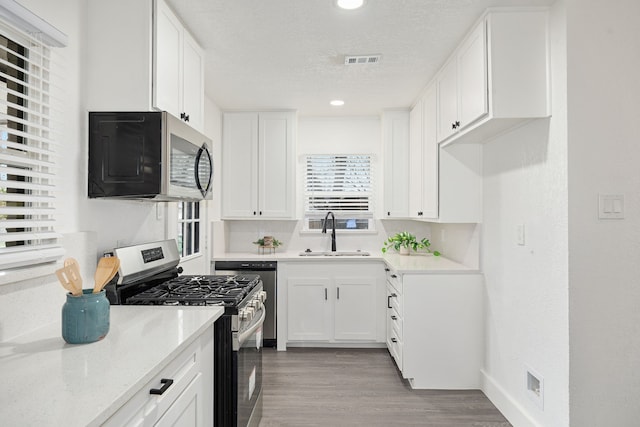 kitchen featuring stainless steel appliances, visible vents, white cabinetry, a sink, and light wood-type flooring